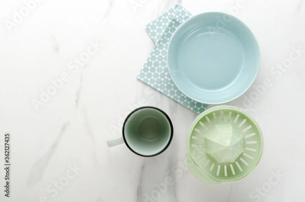 Fototapeta Top view of blue bowl, ceramic cup and handle juicer, napkin on the whte marble table.Empty space