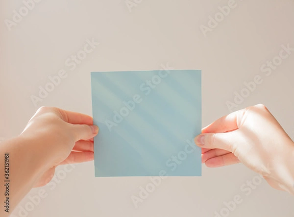 Fototapeta  Blue square leaflet with hard shadows mock up on a white background in the hand of a young woman. School concept