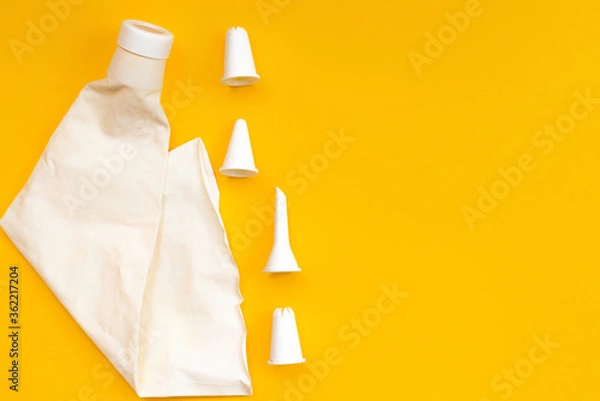 Obraz Empty White pastry bag and nozzles lie on a yellow background. The view from the top. Creative layout for advertising and cooking blog. Horizontal position.