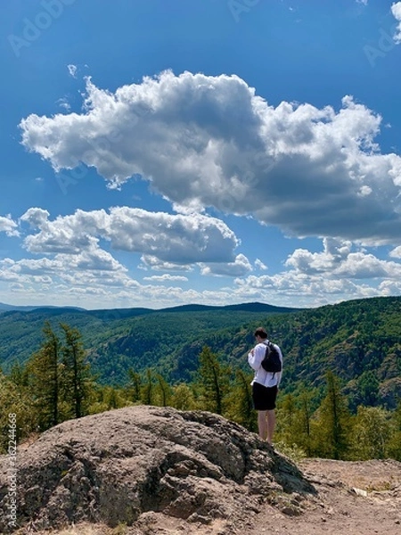 Fototapeta Top view. A young man stands on top of a mountain and enjoys panoramic views of mountains and forests.