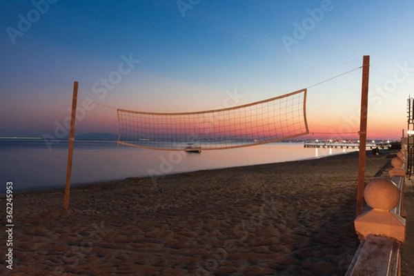 Fototapeta Volleyball net on the beach at sunset with the sea on the background.