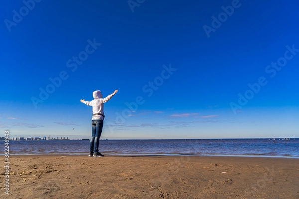 Obraz Silhouette of a woman on the beach from afar. A woman in jeans looks out at the sea at dawn. Space for text.