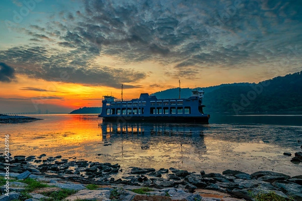 Fototapeta Magnificent view of the sunrise view with an unused ferry floating on the low tide water.