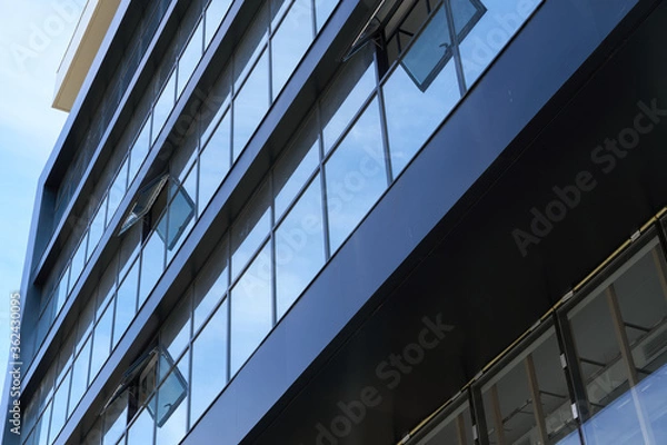 Fototapeta facade of a modern building on a bright Sunny day, blue sky and clouds reflecting in a glass, beautiful exterior of the new building