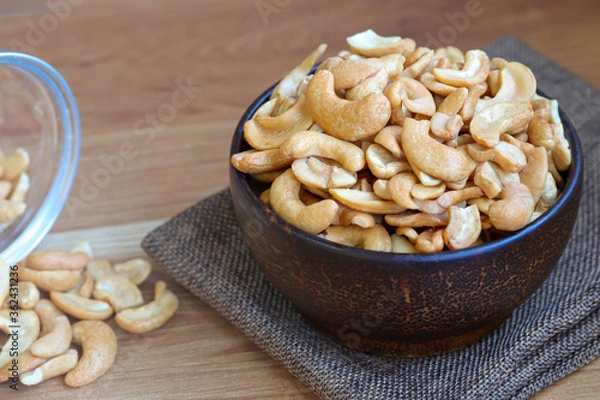 Obraz Cashew nuts peeled in a wooden bowl on table.