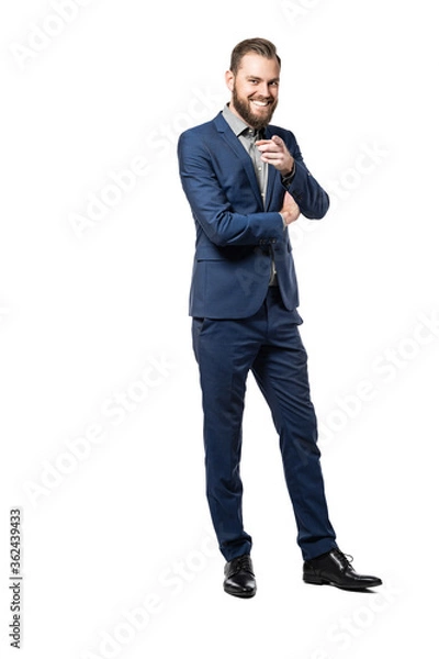 Fototapeta A full body picture of a happy caucasian male smiling and pointing at the camera, wearing a
blue suit standing against a white background.