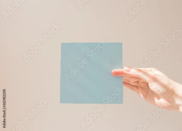 Fototapeta  Blue square leaflet with hard shadows mock up on a white background in the hand of a young woman. School concept
