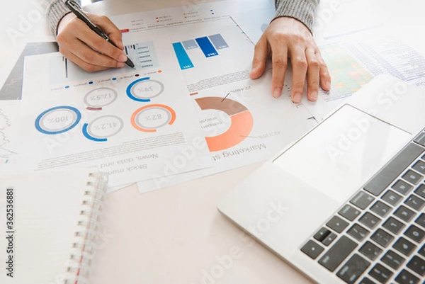 Fototapeta Businesswoman analyze document in his hands.Graphs and diagramm on notebook screen.