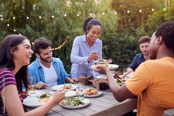 Fototapeta Multi-Cultural Friends At Home Sitting At Table Enjoying Food At Summer Garden Party