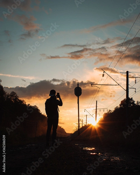 Fototapeta Silhouette of a man standing with phone against the sunset