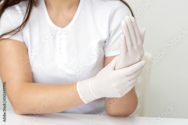 Fototapeta Female hands putting on protective white latex medical gloves during epidemic in quarantine