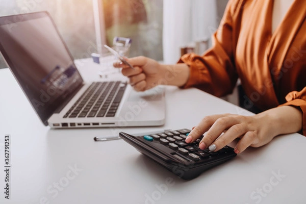 Fototapeta Businesswomen hands working with finances about cost and calculator and laptop with tablet, smartphone at office in morning light