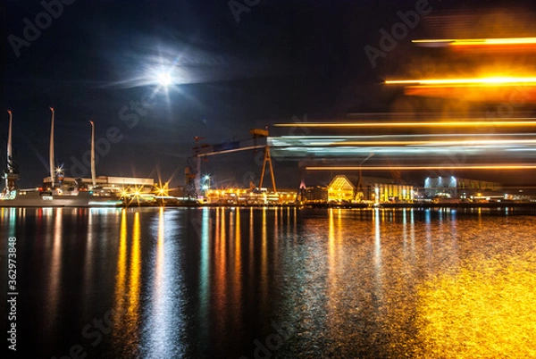 Fototapeta Container Harbor in Kiel Germany for freight transport and shipping of trade exports illuminated at night with bright moon and motion blur