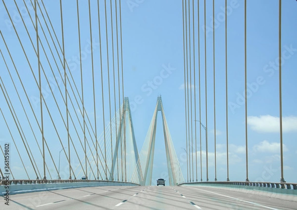 Fototapeta Driving over large cable suspension bridge, with a clear view of the cables and supports and M shaped structure. There is a blue sky and very little traffic. 