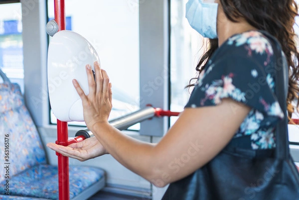 Fototapeta Selective focus on the hands of a woman wearing a mask and putting on hydroalcoholic gel inside a bus.
