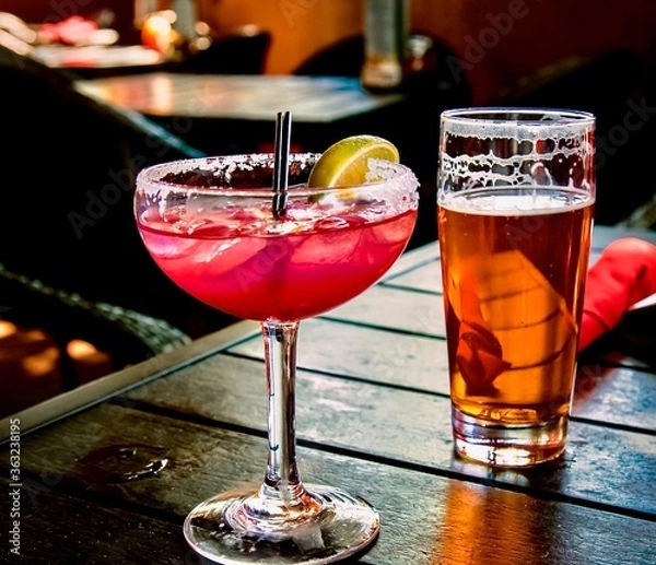 Obraz Refreshing drinks: colorful margarita with lime along with a foamy draught craft beer on a wooden table in a restaurant, ready to be enjoyed.