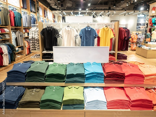 Fototapeta Colorful polo t shirt stack on shelf in large department store shop. Copy space on white sign board.