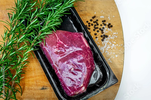 Fototapeta Beef steak in airtight skin packaging and spices on wooden chopping board