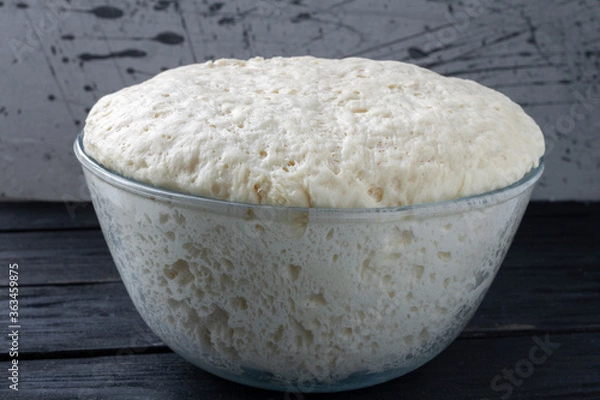 Fototapeta Rising Yeast Dough inglass bowl close up on wooden table