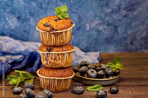 Fototapeta Three fragrant, delicious muffins in the form of a pyramid stand on wooden boards, decorated with blueberries and mint. Horizontal orientation.Backspace.