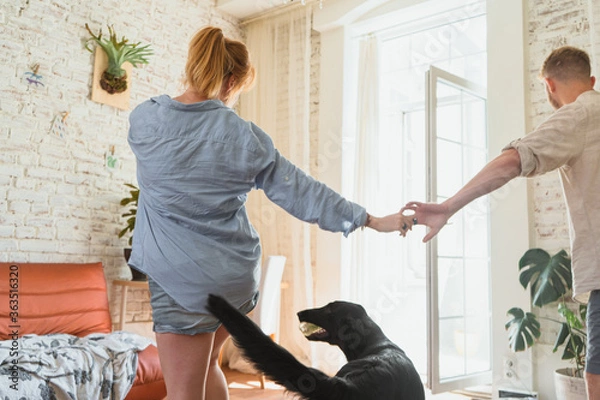 Fototapeta young couple, redhead man and woman are dancing in their flat, couple spending leisure time together and having fun with their dog