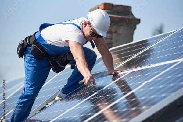 Fototapeta Male workers installing stand-alone solar photovoltaic panel system. Electricians mounting blue solar module on roof of modern house. Alternative energy ecological concept.