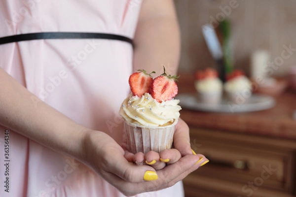 Fototapeta Appetizing cupcake with white cream decorated with fresh strawberries in the hands of a girl.