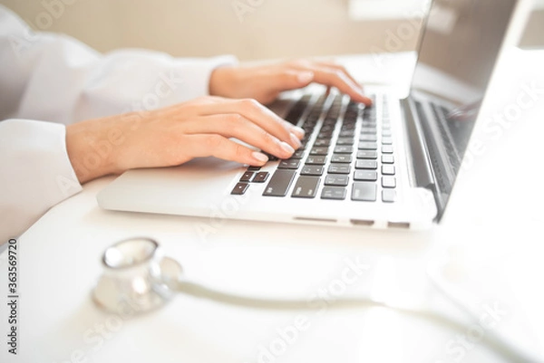 Fototapeta  doctor is typing on a laptop keyboard. online doctor consultation. a stethoscope is on the table. High quality photo