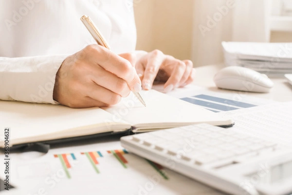 Fototapeta Close up business woman using laptop computer and making note on notepad in modern office.