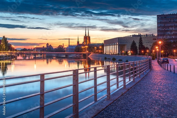 Fototapeta Evening on the boulevards on the Oder river in Wrocław. Illuminated historic buildings and bridges. Beautiful sky, light reflections on blurred water. Two cathedral towers in the distance