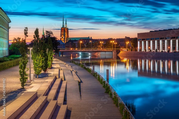 Fototapeta Evening on the boulevards on the Oder river in Wrocław. Illuminated historic buildings and bridges. Beautiful sky, light reflections on blurred water. Two cathedral towers in the distance