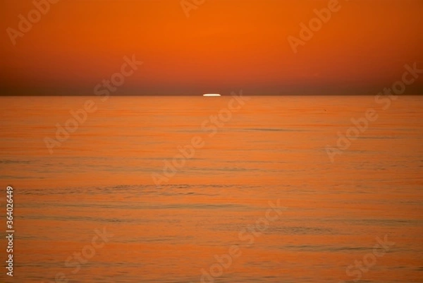 Fototapeta A cold orange sun sets on the North Sea. Fall. Cold evening. Photo from the side of the ship.