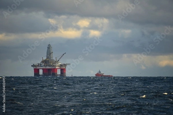 Fototapeta Drilling platform at sea. Extraction of minerals on the shelf. A huge red platform rises above the water. The ship is nearby. Hydrocarbon energy. 