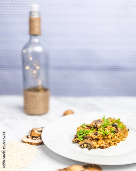 Fototapeta Mushroom risotto with Parmesan cheese and white Wine in a white serving plate on a white marble table with risotto Rice and raw mushroom on the side. Free space for your text/decoration.