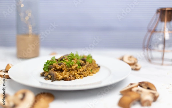 Fototapeta Mushroom risotto with Parmesan cheese and white Wine in a white serving plate on a white marble table with risotto Rice and raw mushroom on the side. Free space for your text/decoration.