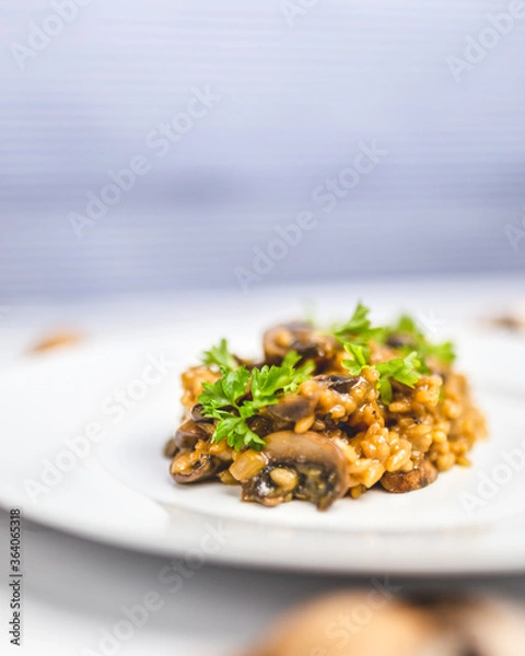 Fototapeta Mushroom risotto with Parmesan cheese and white Wine in a white serving plate on a white marble table with risotto Rice and raw mushroom on the side. Free space for your text/decoration.