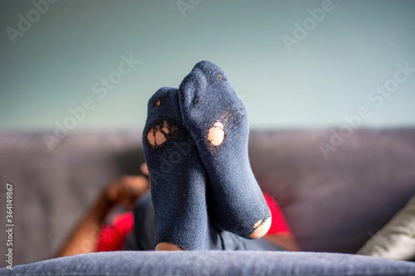 Fototapeta Bottom of old worn out socks with holes in it. Man in living room with feet propped up on ottoman, relaxing on the couch at home. Concept of poverty
