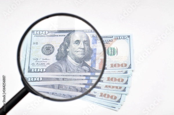 Obraz Magnifying glass and dollars on a white background. 100 dollars banknote view through a magnifying glass
