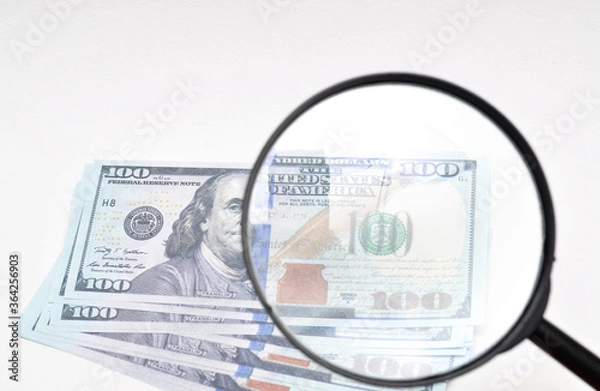 Obraz Magnifying glass and dollars on a white background. 100 dollars banknote view through a magnifying glass