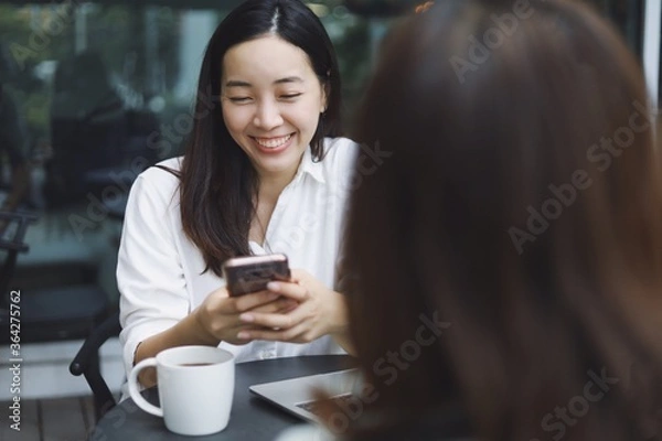 Fototapeta Woman smiling using smart phone in coffee shop.