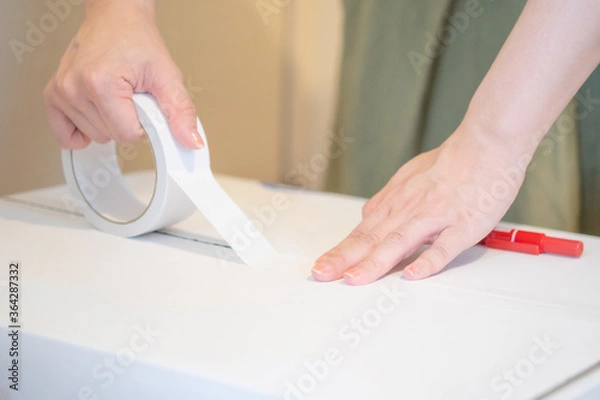 Fototapeta ダンボールにガムテープでフタをする女性の手、引越しの荷造りのイメージ