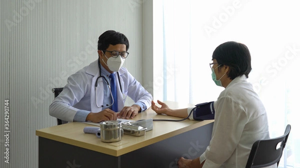 Fototapeta asian doctor using automated digital sphygmomanometer to measure blood pressure of senior woman patient that visit at the hospital because of hypertension. healthcare and medical concept