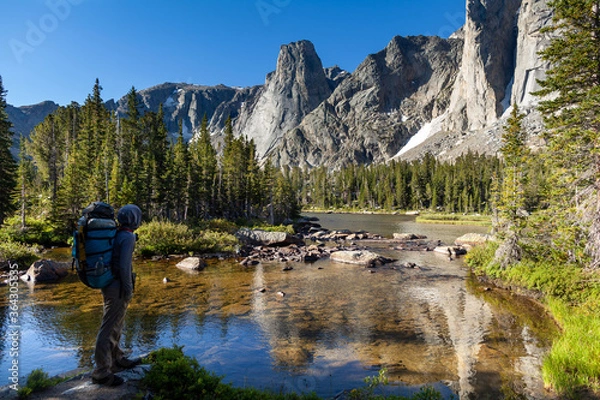 Fototapeta Mężczyzna z plecakiem podróżujący North Fork Trail zatrzymuje się nad rzeką North Popo Agie, aby podziwiać widok na jezioro i cyrk po północnej stronie Big Sandy Mountain w Wind River Range, WY.