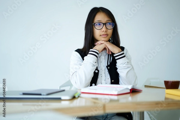 Fototapeta Contemplative hipster girl with eyeglasses thoughtfully thinking about new ideas for writing interesting story in homework task sitting at table with modern technology and notebook for noting