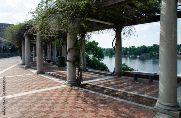Fototapeta A section of the Augusta river walk with a shaded rest area under a pergola, with white columns. There is a view of the Savannah river.