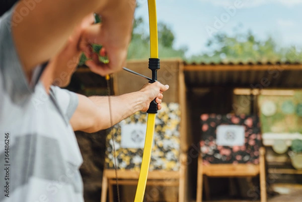 Fototapeta Archer holds yellow bow aiming at a target, during a open air corporate team building.  Outdoor leisure activity concept