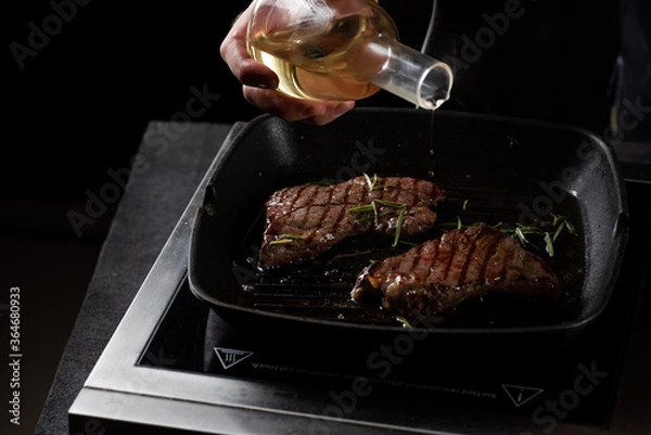 Fototapeta the chef pours butter on a beef steak in a frying pan