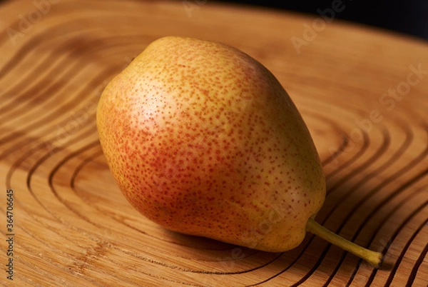 Fototapeta The red-yellow pear lies on a wooden stand on a black background