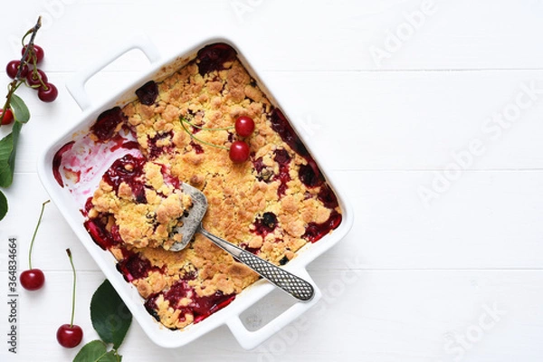 Fototapeta Homemade summer dessert with cherries. Crumble with cherries in a baking dish on a white background.