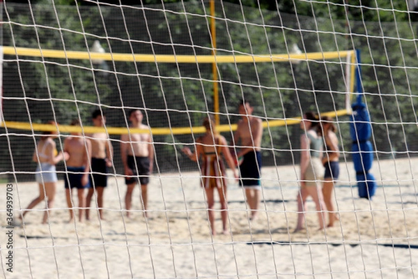Obraz Beach volleyball, summer sport. View through a rope net to people playing ball in the sand, selective focus